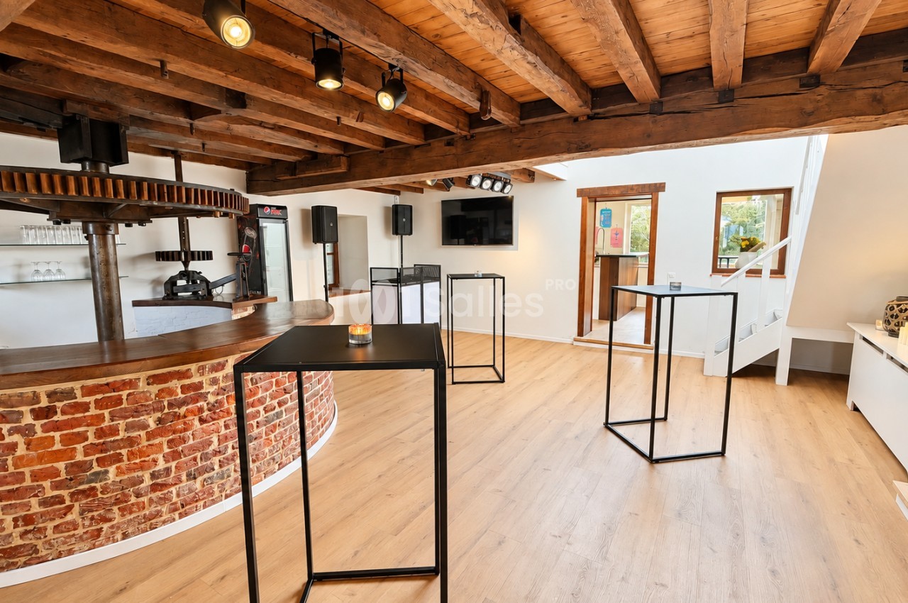 Salle aux poutres apparentes avec bar courbe en briques rouges, mange-debout en métal noir et sol en parquet clair, sans mobilier de réception dressé.