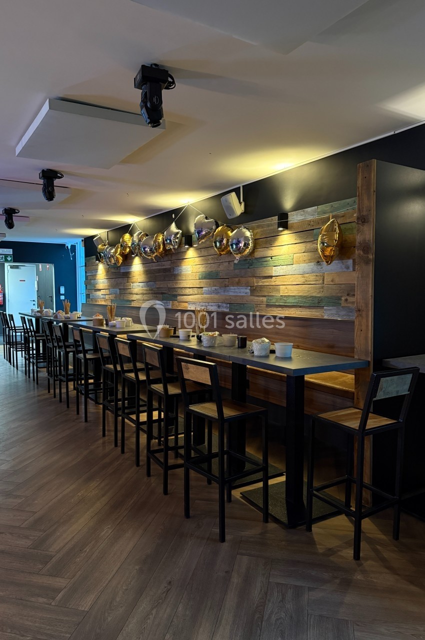 Long comptoir en bois avec des tabourets hauts, éclairé par des lampes murales, dans un espace intérieur moderne.