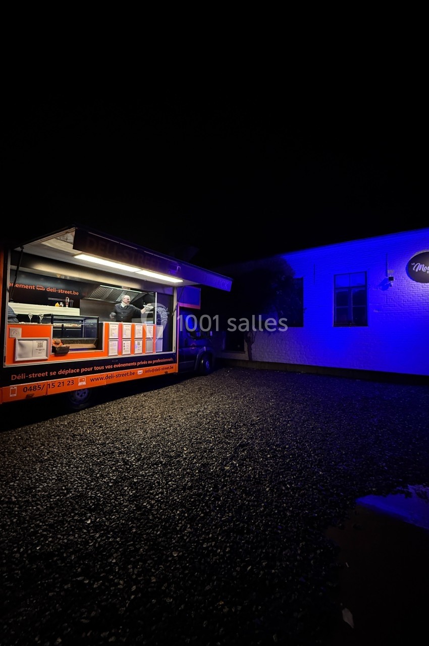 Camion de restauration éclairé la nuit, stationné devant un bâtiment illuminé par une lumière bleue.