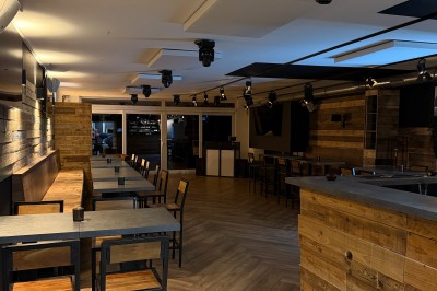 Salle lumineuse avec parquet clair, table et chaises au centre, escalier blanc, machine à coudre ancienne et tableau au mur.