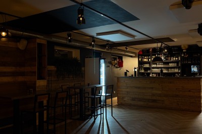Salle lumineuse avec parquet clair, table et chaises au centre, escalier blanc, machine à coudre ancienne et tableau au mur.