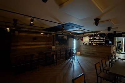 Salle lumineuse avec parquet clair, table et chaises au centre, escalier blanc, machine à coudre ancienne et tableau au mur.