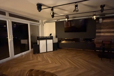 Salle lumineuse avec parquet clair, table et chaises au centre, escalier blanc, machine à coudre ancienne et tableau au mur.