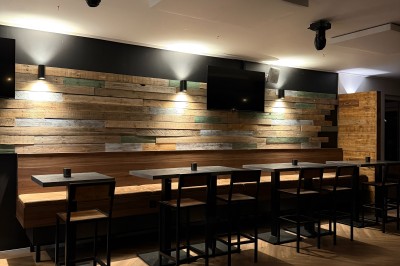 Salle lumineuse avec parquet clair, table et chaises au centre, escalier blanc, machine à coudre ancienne et tableau au mur.