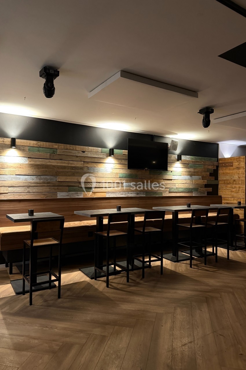 Salle moderne avec un long comptoir en bois, des tabourets noirs, un mur en bois et un écran mural.