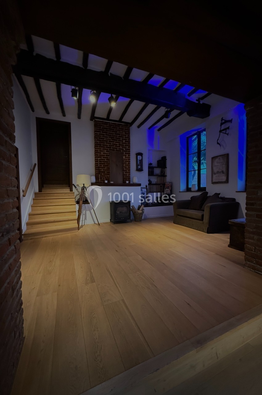 Salon chaleureux avec parquet en bois, murs en briques, poêle à bois, canapé et éclairage tamisé.