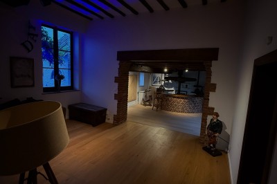 Salle lumineuse avec parquet clair, table et chaises au centre, escalier blanc, machine à coudre ancienne et tableau au mur.