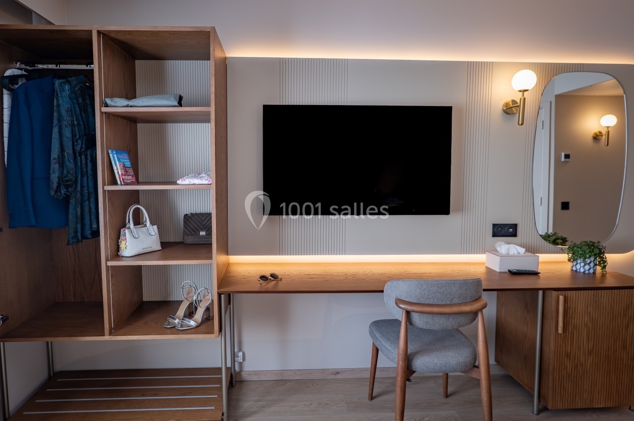 Bureau en bois avec chaise, télévision murale, étagères ouvertes contenant des vêtements et accessoires, éclairage moderne.