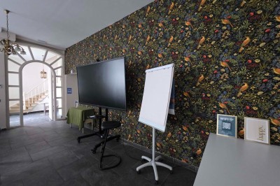 Salle de réunion lumineuse avec de longues tables blanches, chaises noires, écran mural et tableau blanc.