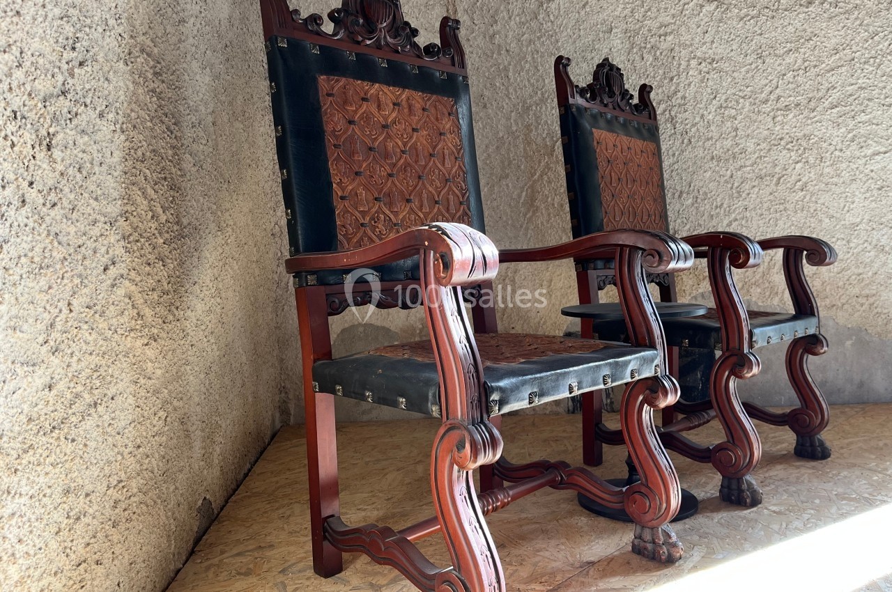 Deux fauteuils en bois sculpté avec assise et dossier en cuir décoré, placés contre un mur texturé.