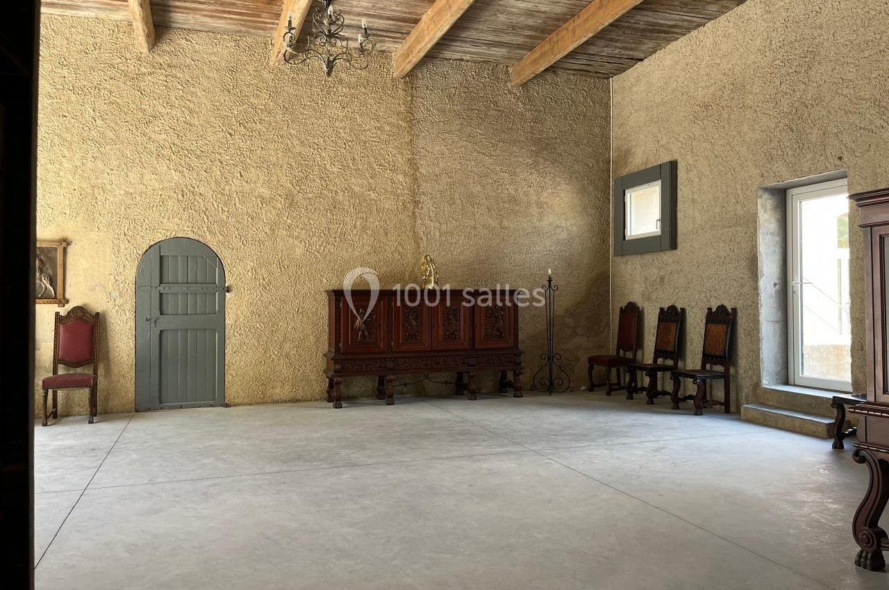 Salle avec murs en pierre beige, plafond en poutres apparentes, mobilier ancien en bois et lumière naturelle.