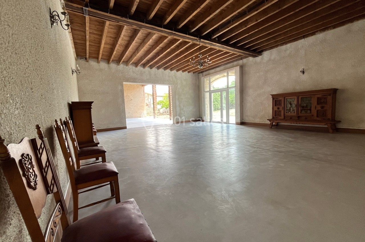 Salle spacieuse avec sol en béton, plafond en poutres apparentes, chaises alignées et meuble en bois contre un mur.