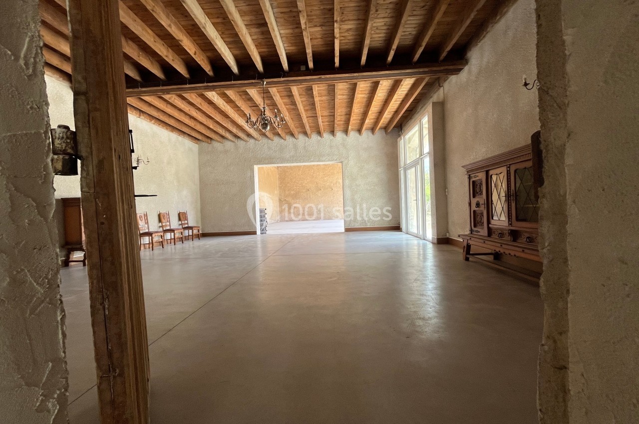 Salle spacieuse avec plafond en bois, murs clairs, sol en béton lisse et mobilier ancien le long des murs.