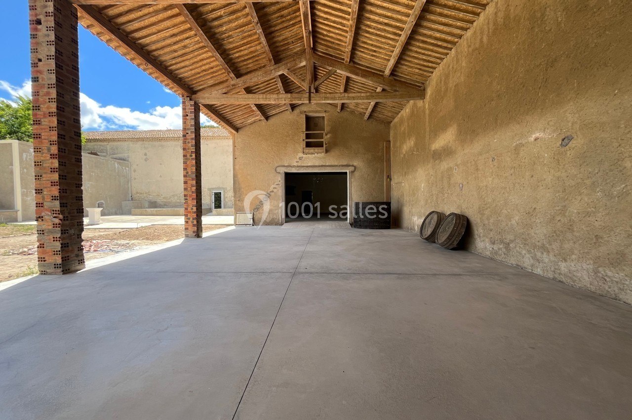 Intérieur d'un hangar en pierre avec toit en bois, sol en béton et quelques pneus empilés contre un mur.