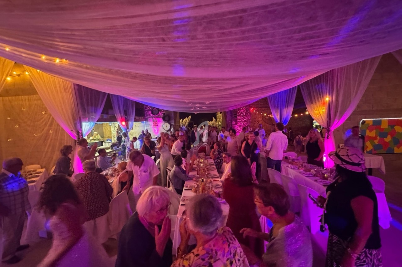 Salle décorée avec des voilages et éclairages colorés, remplie de convives autour de tables lors d’un événement festif.