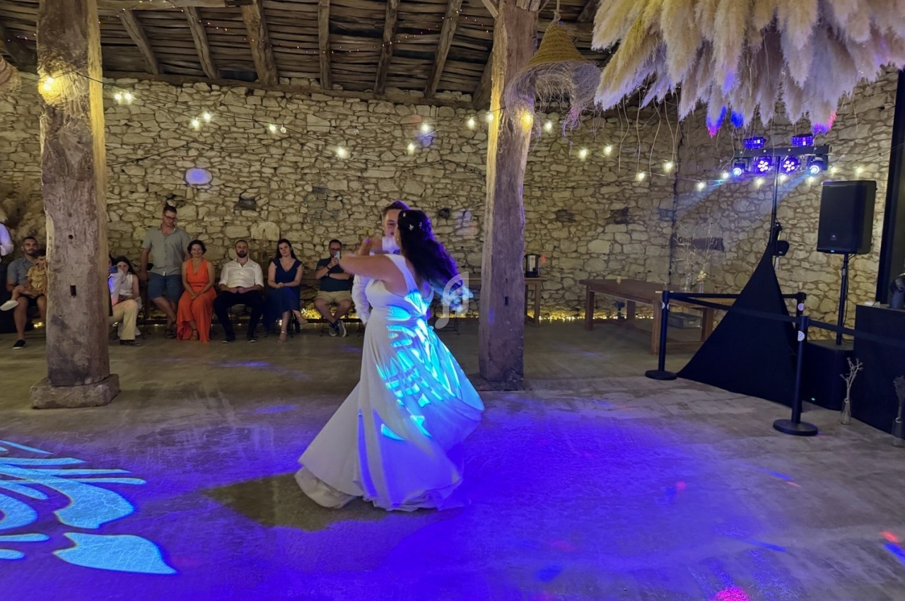 Une mariée danse sous des lumières colorées dans une grange en pierre décorée de pampas et guirlandes lumineuses.
