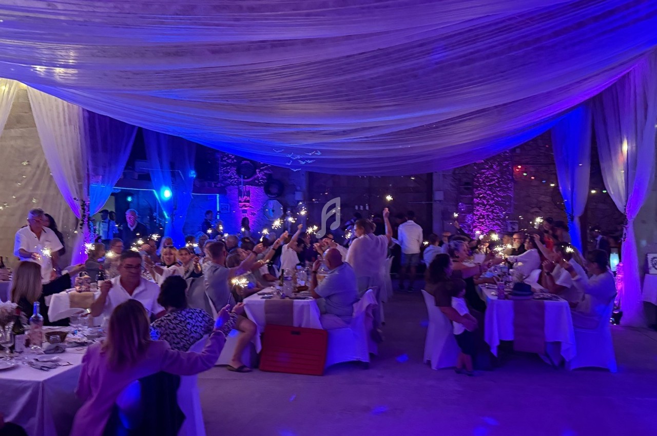 Des convives assis à des tables dans une salle décorée, levant des lumières dans une ambiance festive et tamisée.