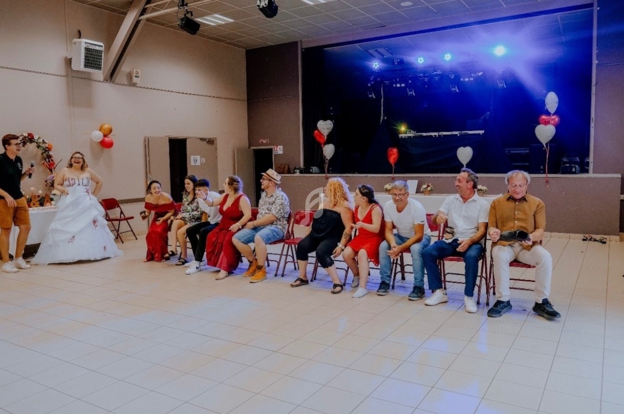 Un groupe de personnes assises dans une salle décorée, avec une scène éclairée et des ballons en arrière-plan.