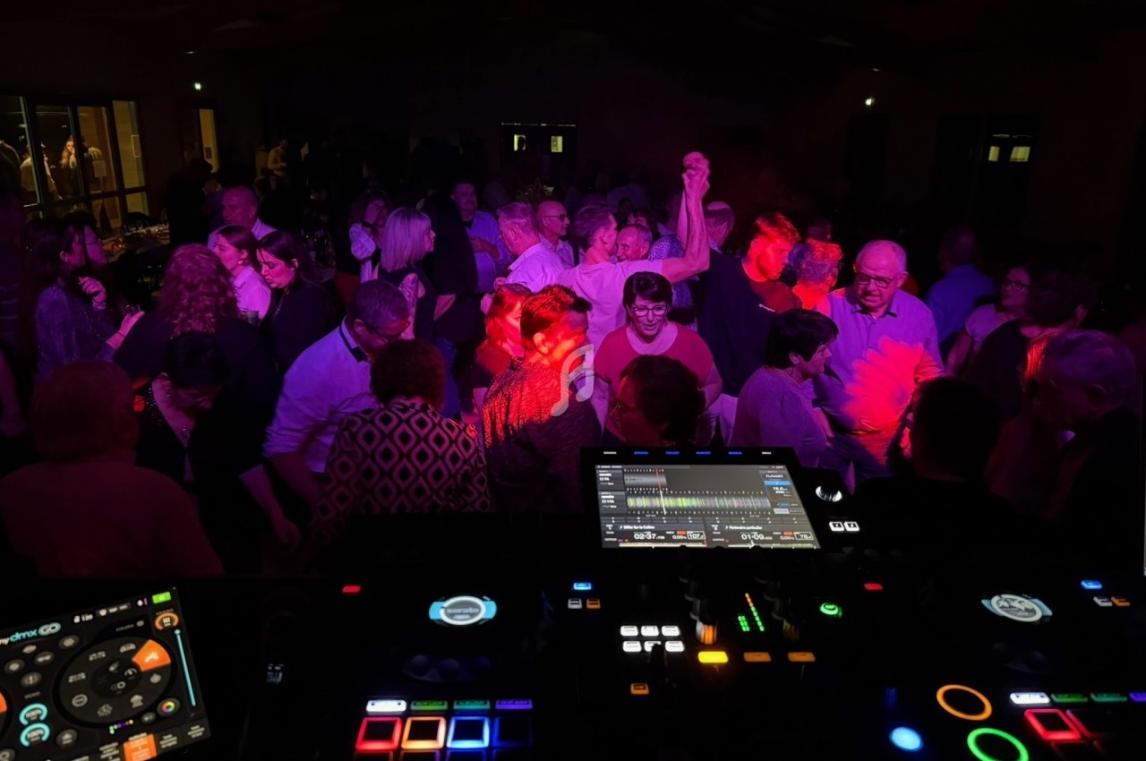 Vue d'une piste de danse animée avec des lumières colorées, prise depuis une table de mixage en premier plan.