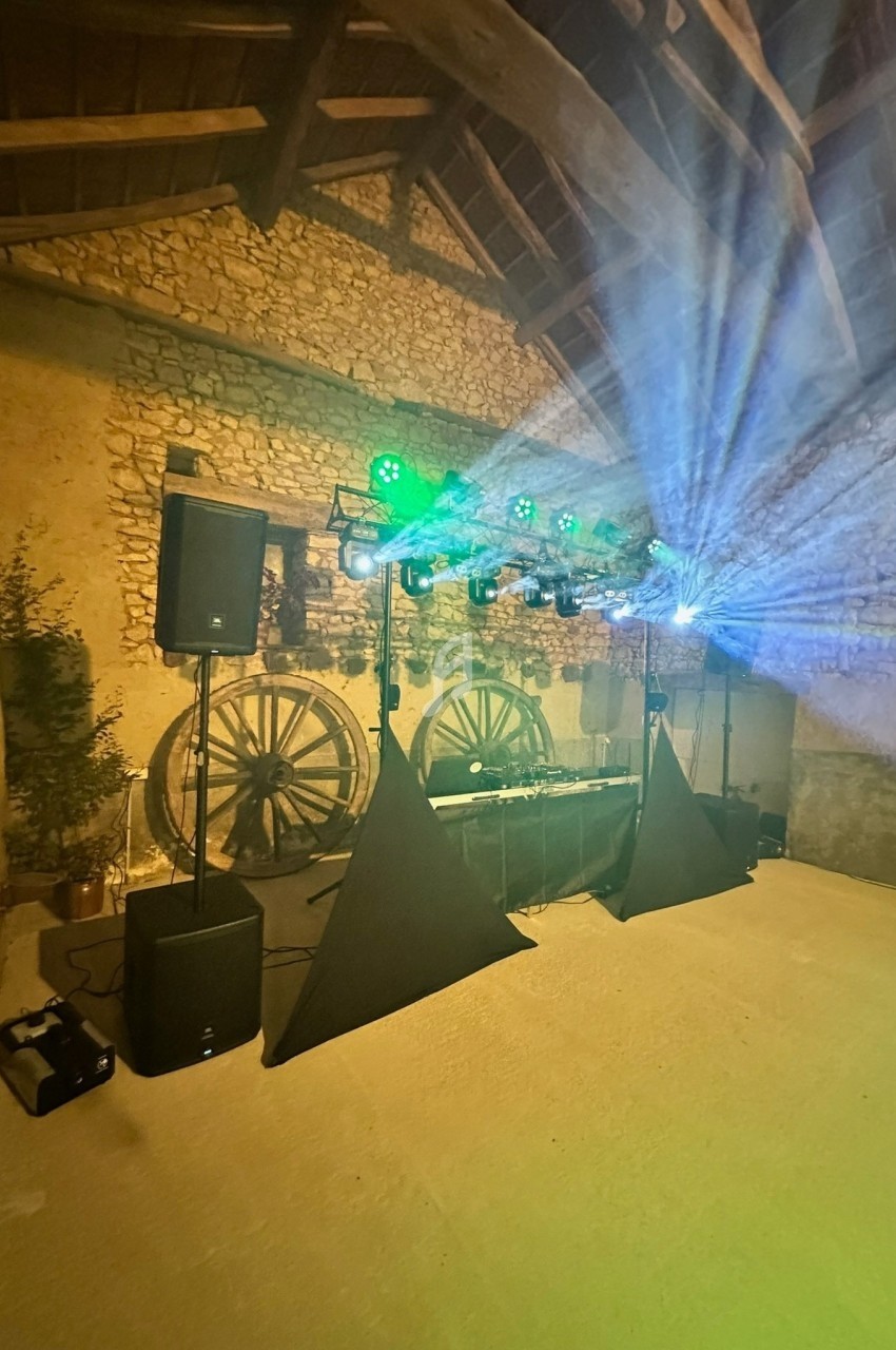 Installation de matériel de sonorisation et éclairage avec jeux de lumière dans une salle en pierre avec charpente apparente.