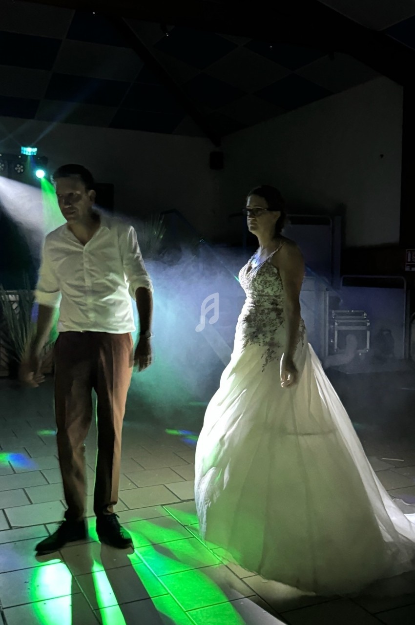 Un couple danse sous des lumières colorées et des effets de fumée dans une salle sombre.