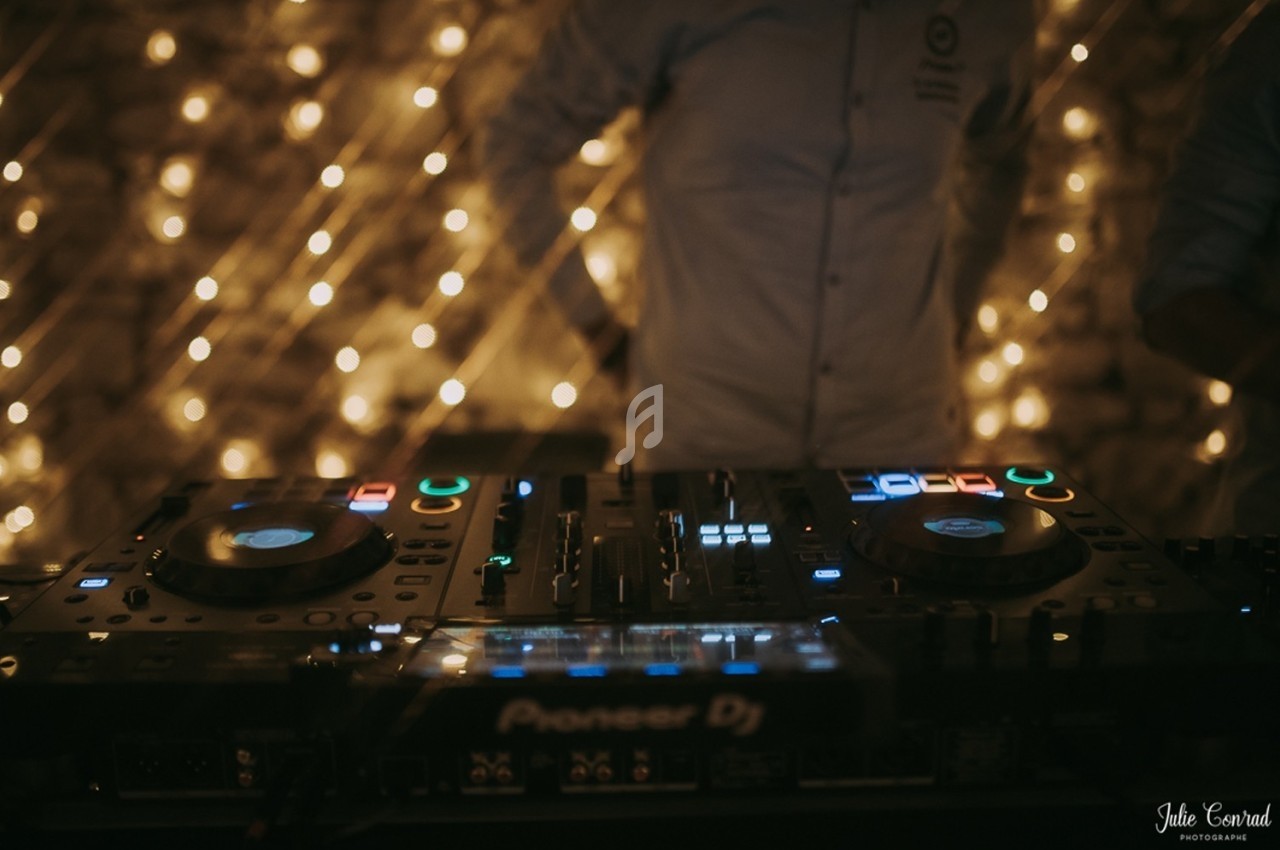 Console de mixage DJ éclairée, avec des lumières floues en arrière-plan dans une ambiance tamisée.