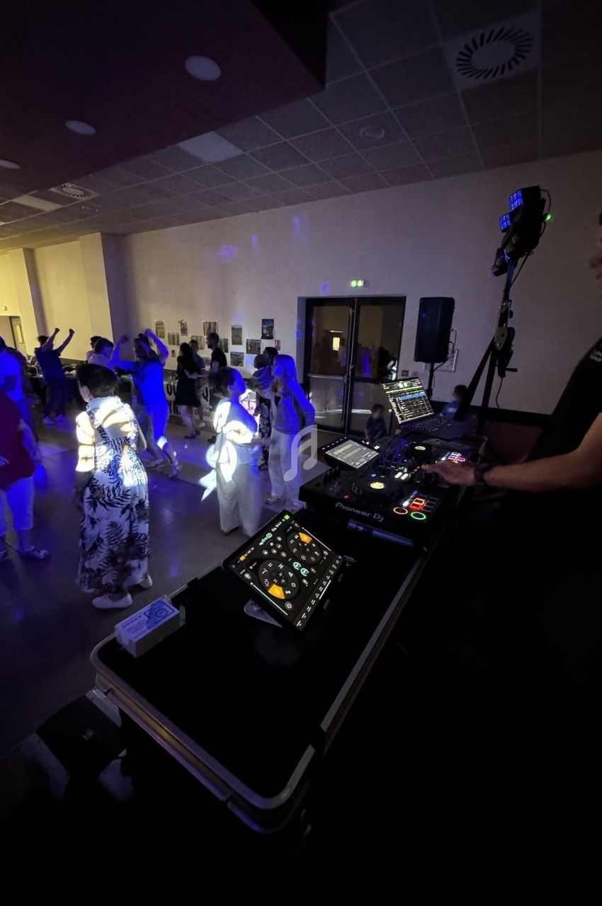 Un DJ anime une soirée dansante dans une salle éclairée par des lumières colorées, avec des participants sur la piste.