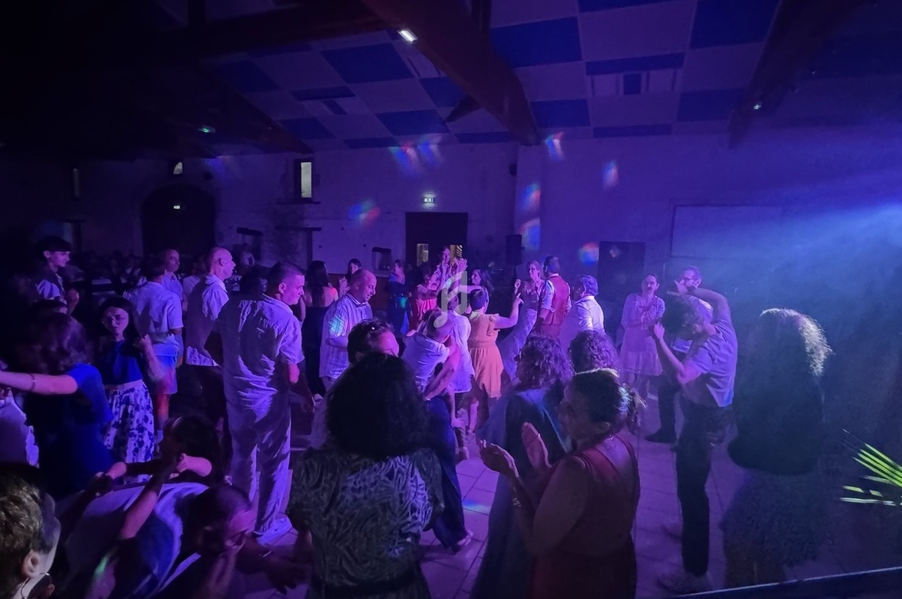Groupe de personnes dansant dans une salle éclairée par des lumières colorées, ambiance festive en soirée.