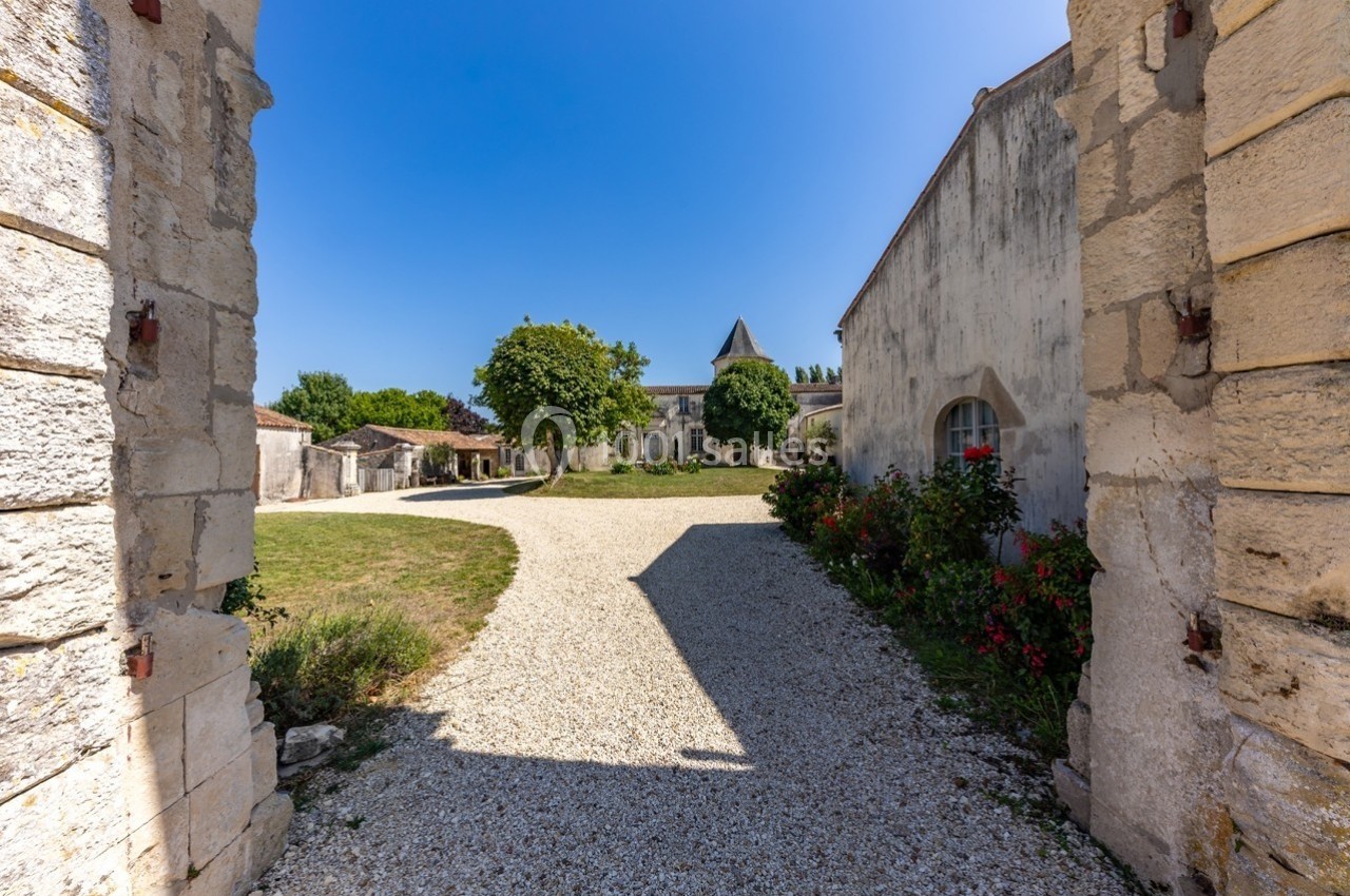 Cour intérieure avec allée en gravier, entourée de bâtiments en pierre et d'arbres sous un ciel bleu dégagé.