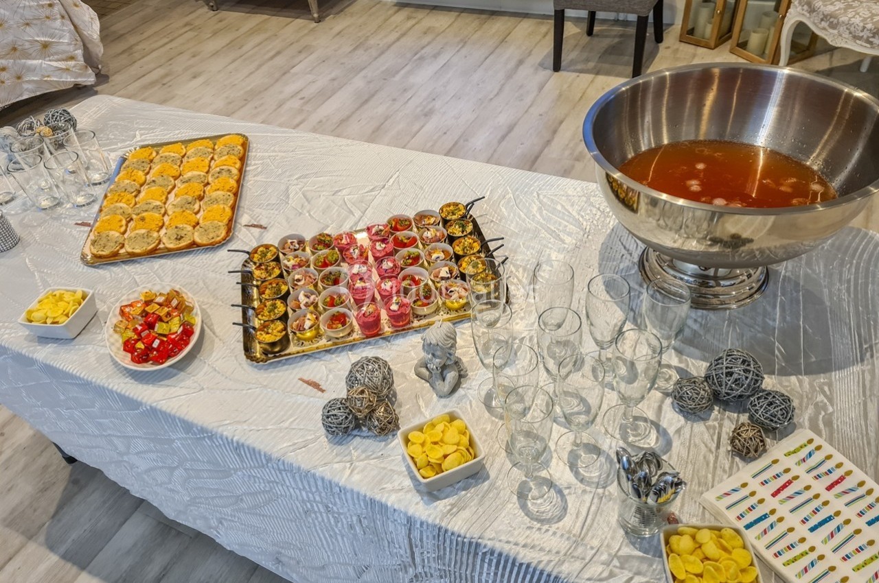 Buffet avec verrines, amuse-bouches, bols de snacks et une grande coupe de punch sur une table blanche.