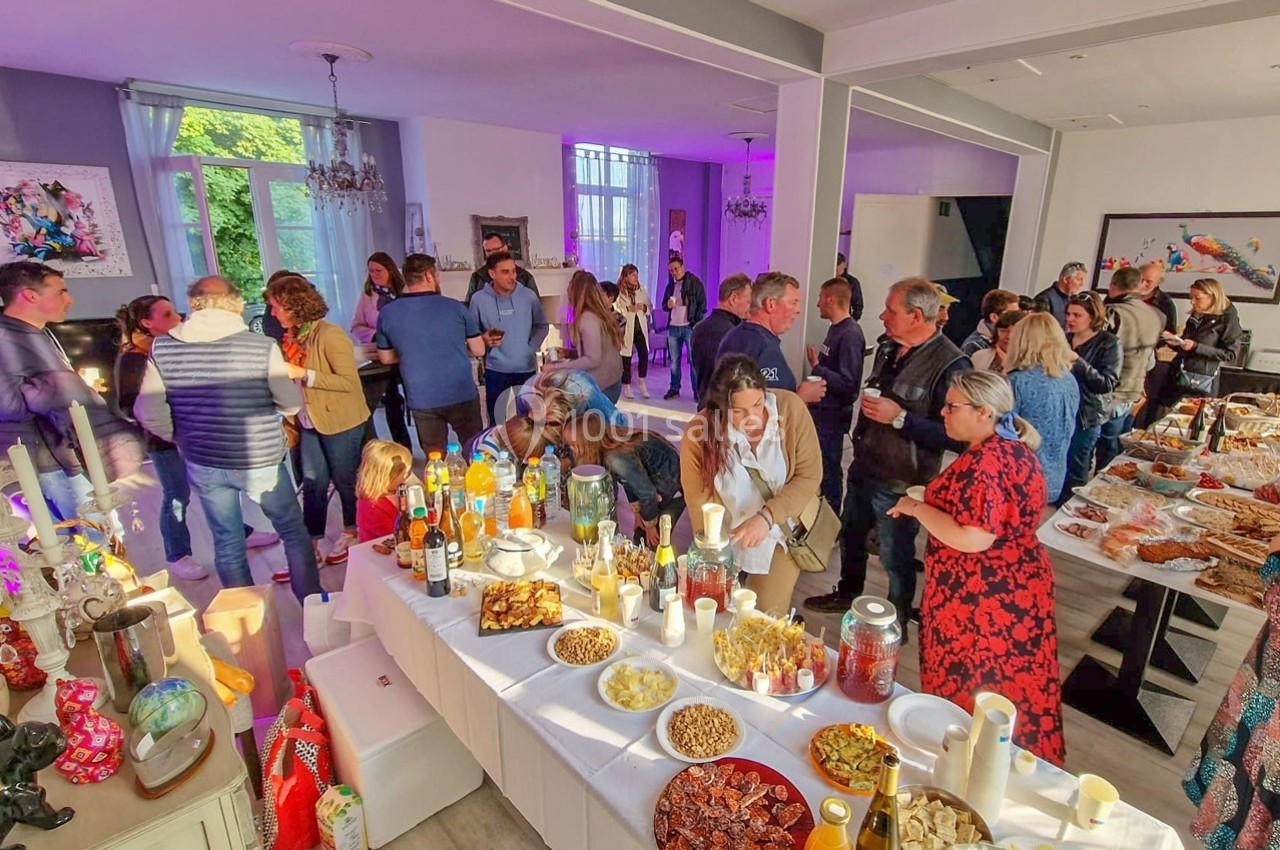 Groupe de personnes réunies dans une salle lumineuse autour d'un buffet varié avec boissons et plats.