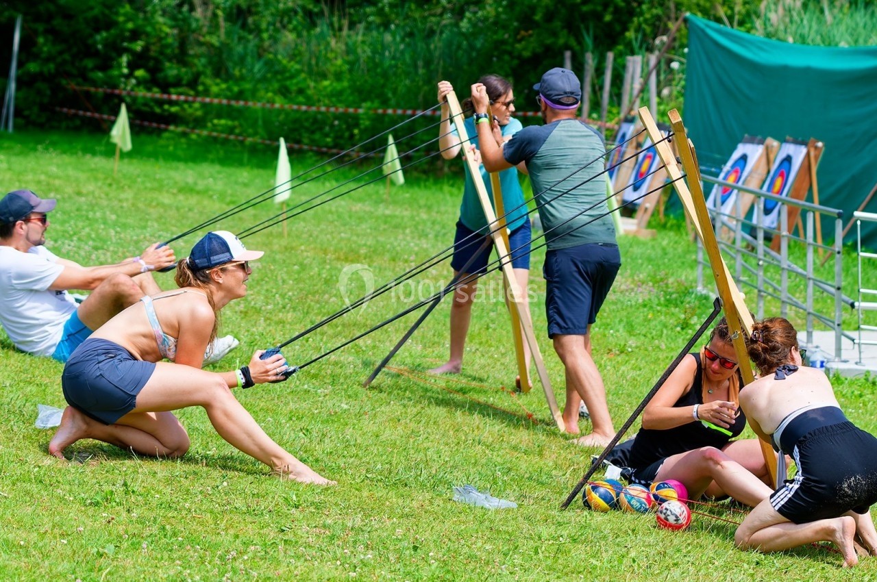 Des personnes utilisent des lance-pierres géants pour propulser des balles sur une pelouse lors d'une activité en plein air.