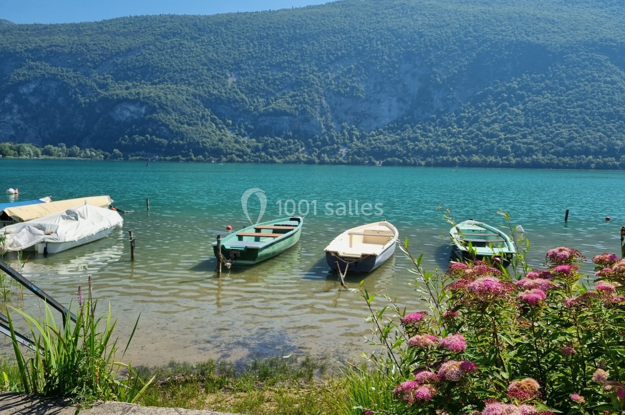 Quatre barques amarrées sur un lac turquoise entouré de montagnes verdoyantes, avec des fleurs au premier plan.