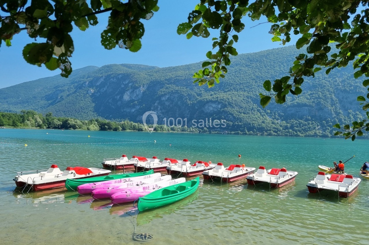 Pédalos et kayaks colorés amarrés sur un lac entouré de montagnes verdoyantes par une journée ensoleillée.
