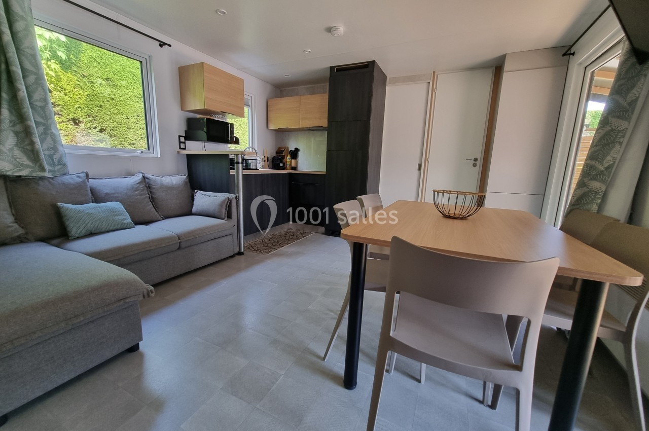 Intérieur lumineux d'un mobil-home avec salon, table à manger, cuisine équipée et grandes fenêtres donnant sur l'extérieur.