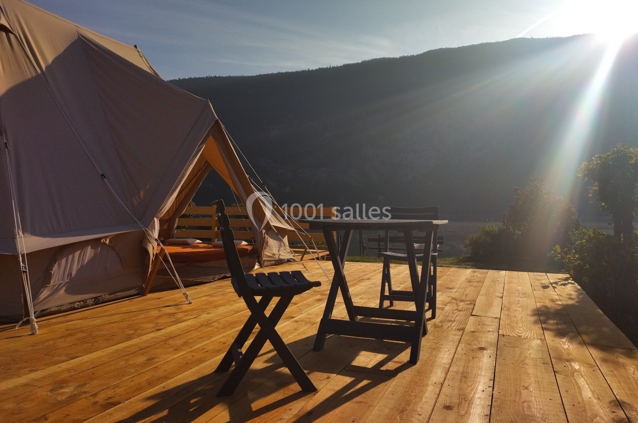 Tente en toile et mobilier de jardin en bois sur une terrasse ensoleillée avec vue sur des montagnes.