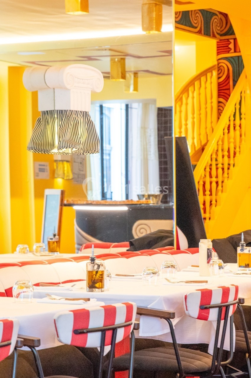 Salle de restaurant lumineuse avec tables dressées, chaises rayées rouges et blanches, et décorations colorées.