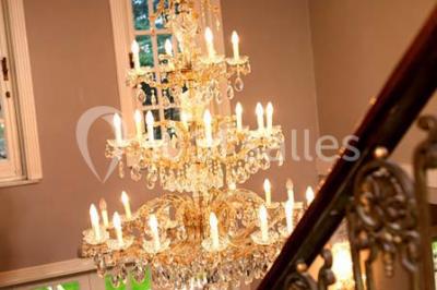 Lustre en cristal allumé suspendu au-dessus d'un escalier avec rampe en fer forgé et sol en marbre.