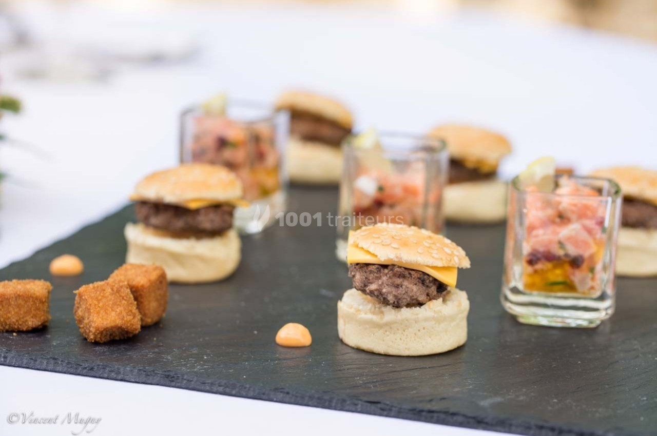 Plateau de dégustation avec mini-burgers, verrines de tartare et cubes panés sur une ardoise noire.