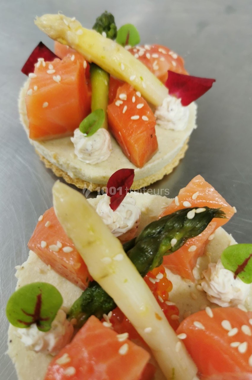 Deux tartelettes garnies de saumon, asperges vertes et blanches, crème et décorations végétales sur une base croustillante.