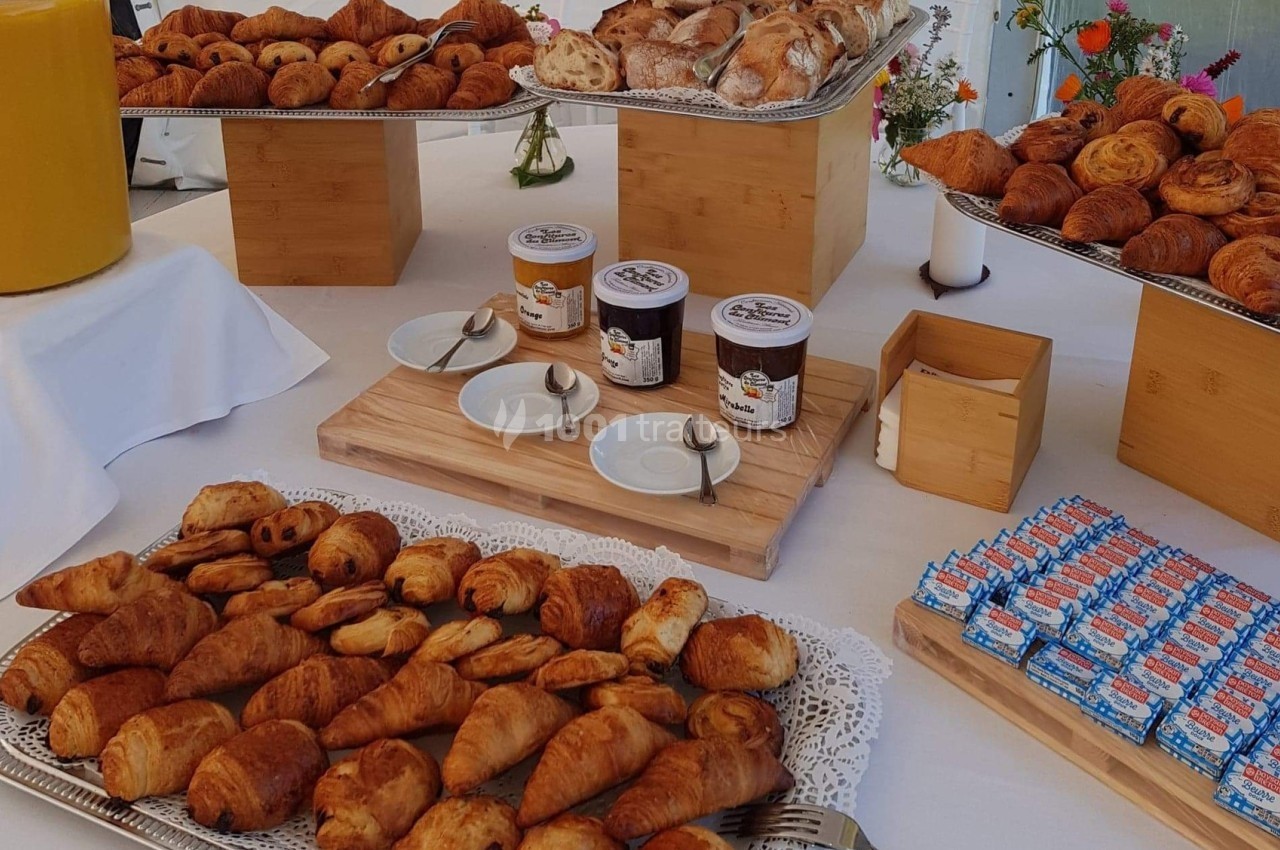 Plateau de viennoiseries variées avec confitures, jus d'orange et décor floral sur une table dressée.