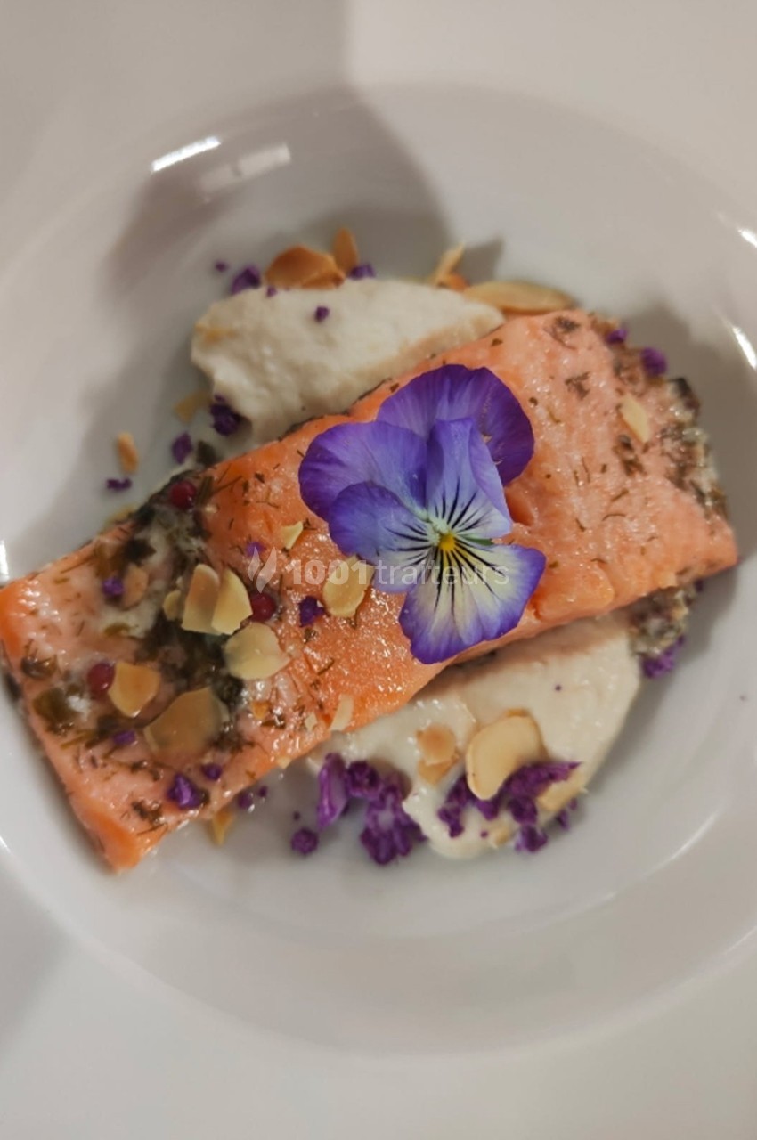Filet de saumon garni d'amandes effilées, fleurs comestibles et purée blanche, présenté dans une assiette blanche.