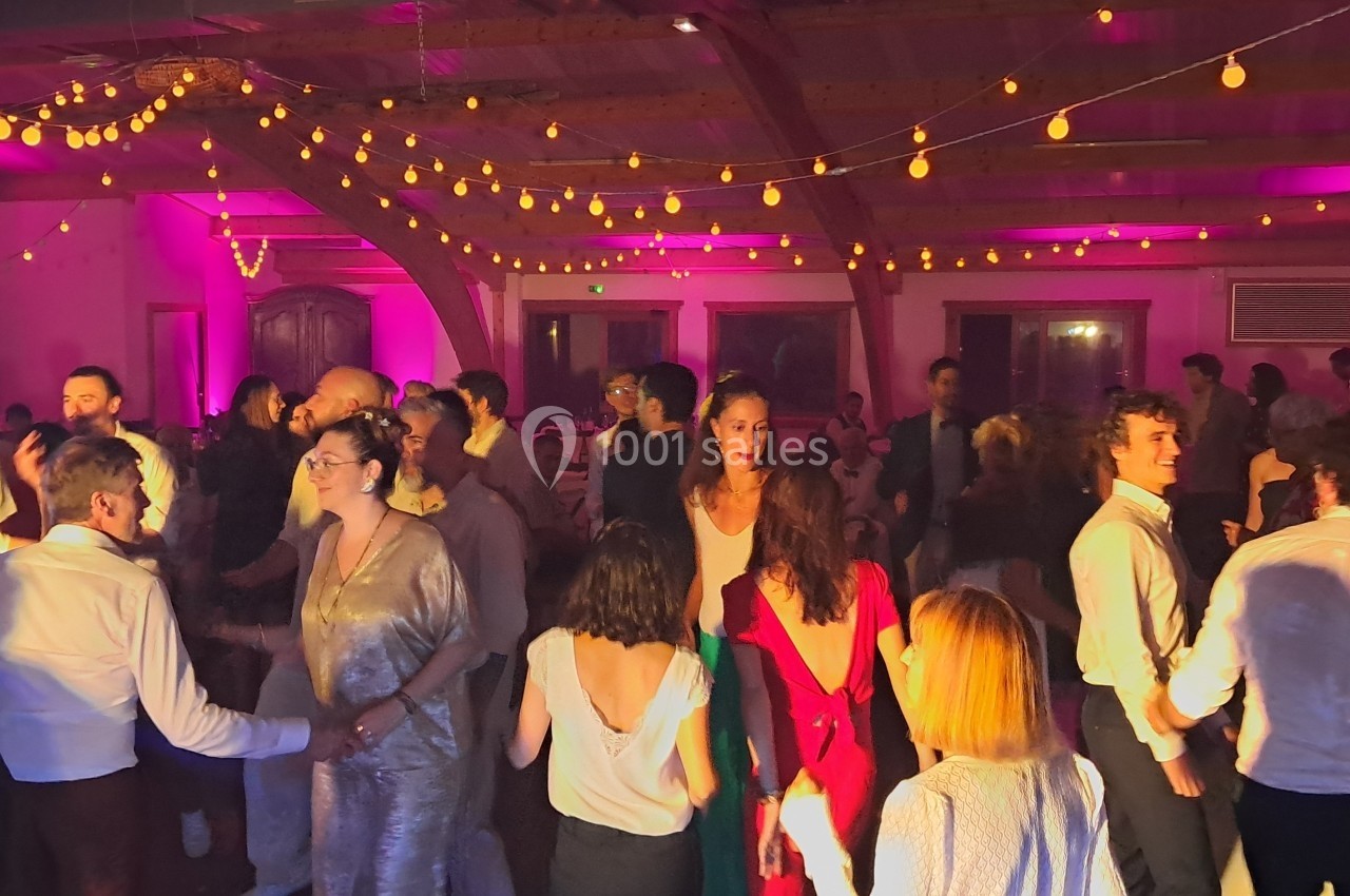 Des personnes dansent dans une salle éclairée par des guirlandes lumineuses et une lumière rose.