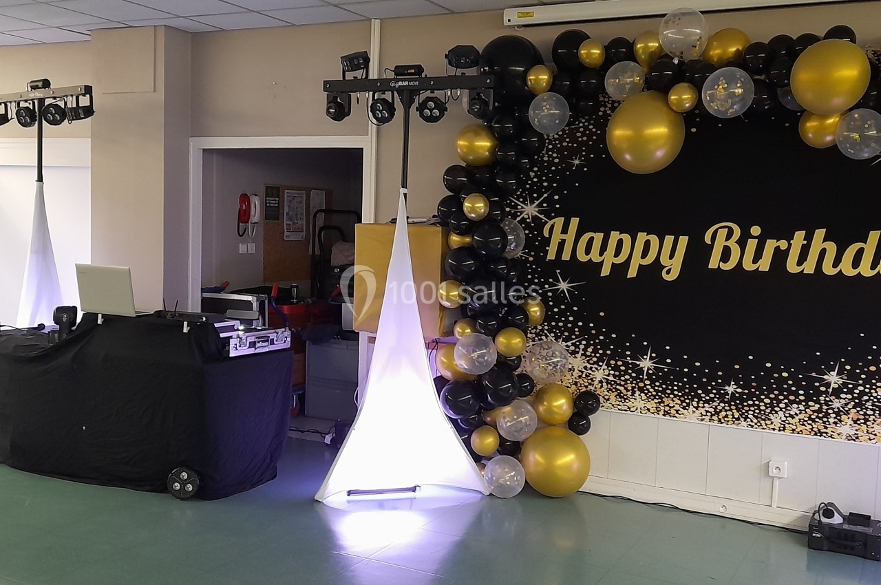 Décoration d'anniversaire avec ballons noirs, dorés et blancs, panneau ’Happy Birthday’ et matériel de sonorisation installé.