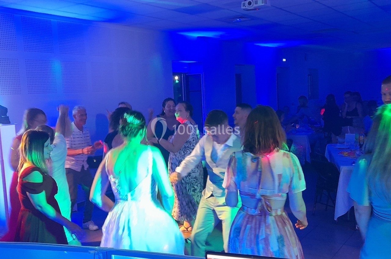 Des personnes dansent dans une salle éclairée par des lumières colorées lors d'un événement festif.