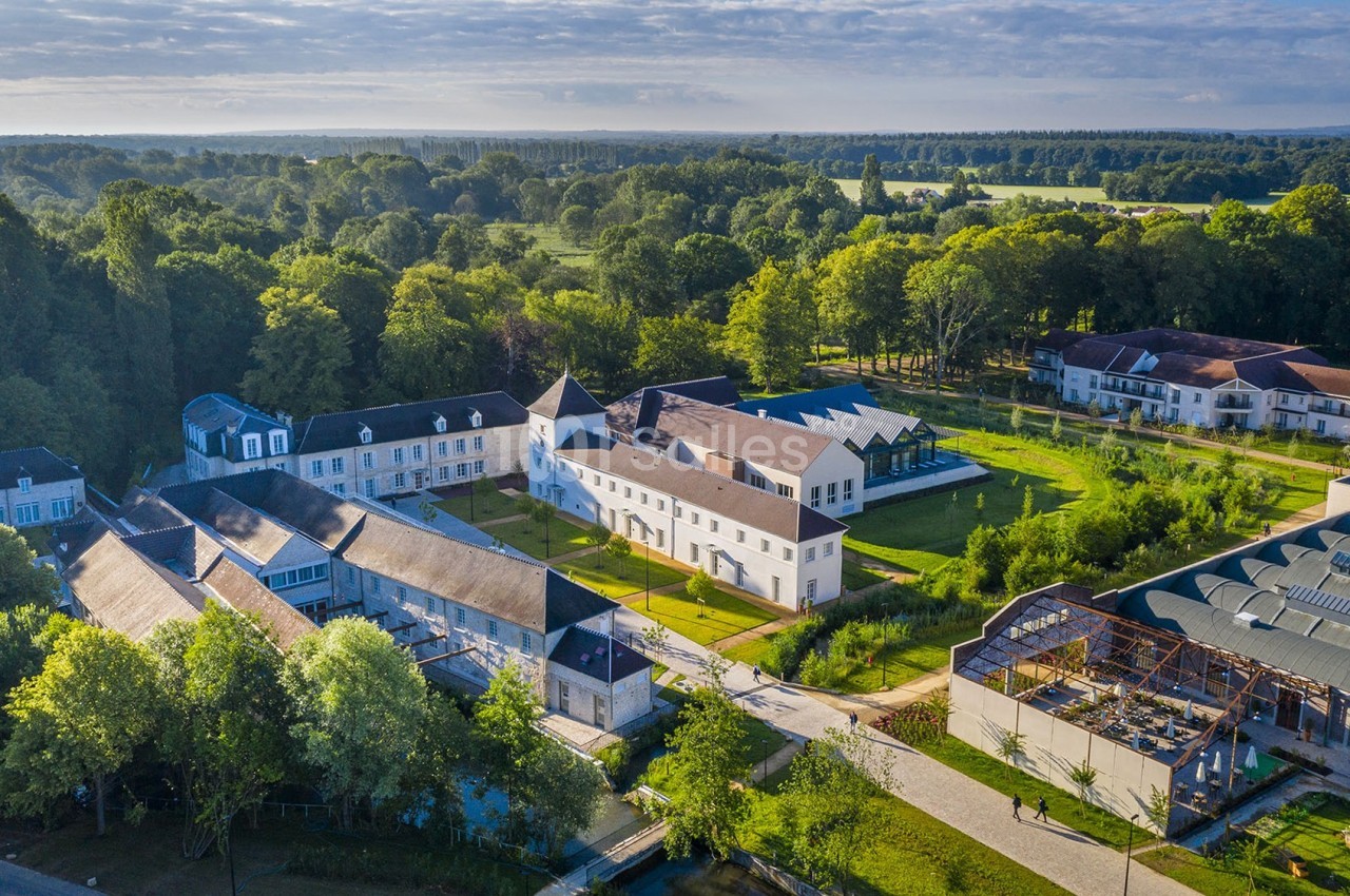Vue aérienne d'un domaine avec bâtiments anciens rénovés, entouré de verdure et de paysages champêtres.
