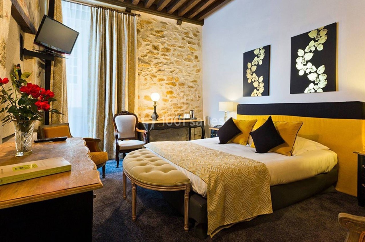 Chambre lumineuse avec lit double, murs en pierre, mobilier classique, et décoration élégante.