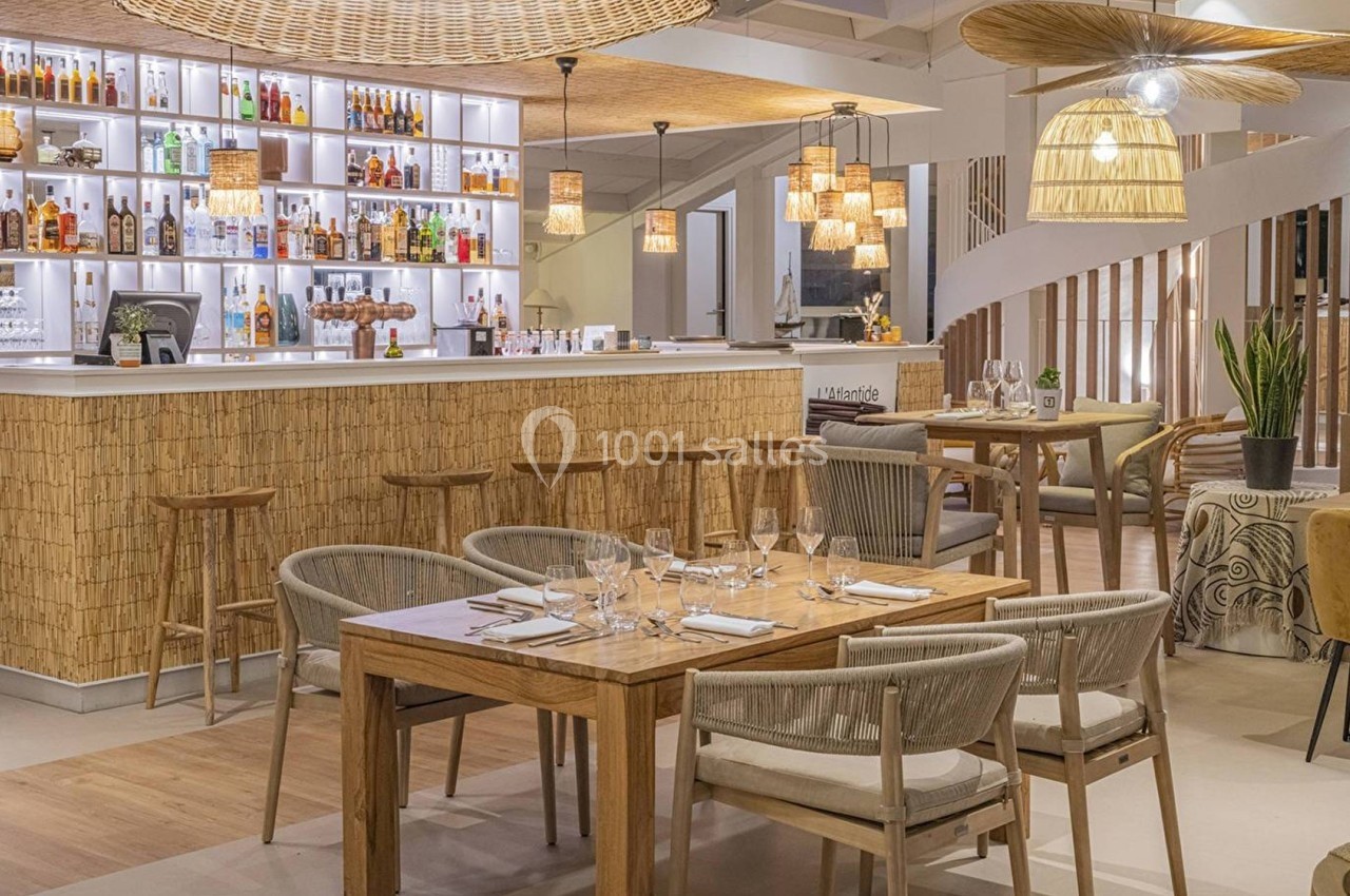 Salle de restaurant moderne avec bar en arrière-plan, mobilier en bois, éclairage chaleureux et décoration naturelle.