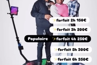 Borne photo avec éclairage, écran et accessoires humoristiques posés devant un mur végétal.