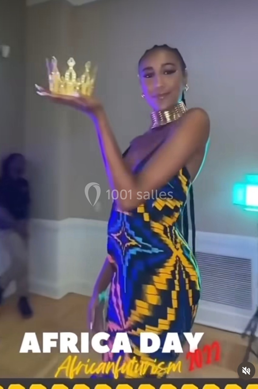 Femme en robe colorée tenant une couronne dorée dans une main, lors d'un événement en intérieur.